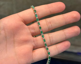 May include: A delicate gold bracelet featuring a series of oval-cut emeralds and small, sparkling diamonds. The gemstones are set closely together, creating a continuous line of green and white. The bracelet is designed for a classic and elegant look.