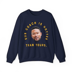 May include: Navy blue sweatshirt with a yellow circle graphic that says "Our Coach Is Hotter Than Yours." Inside the circle is a photo of a man's face.