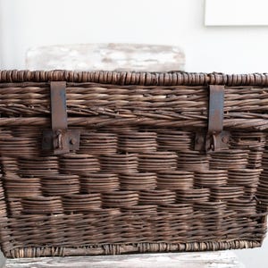 May include: A brown wicker basket with metal clasps and hinges. The basket is woven with a tight, intricate pattern.