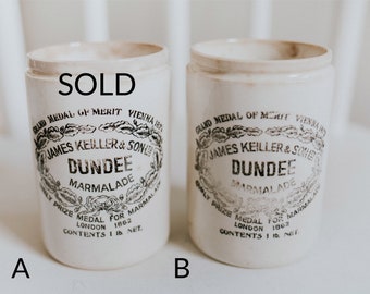 May include: Two vintage white ceramic jars with black lettering. The jars are labeled "GRAND MEDAL OF MERIT VIENNA 1873 JAMES KEILLER & SON LTD DUNDEE MARMALADE DAILY PRIZE MEDAL FOR MARMALADE LONDON 1862 CONTENTS 1 lb NET."