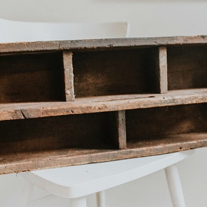 May include: A rustic wooden shelf with multiple compartments, perfect for organizing small items. The shelf is made of reclaimed wood and has a natural, weathered finish.