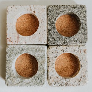 May include: Four square stone candle holders with cork inserts. Each holder has a different pattern of gray, white, and brown.