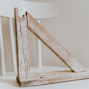 May include: A weathered, whitewashed wooden shelf bracket with a triangular shape. The bracket is made of rough-hewn wood and has a rustic, farmhouse style.