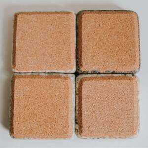 May include: Four square cork coasters with a speckled gray and white pattern. The coasters are made of cork and have a natural, rustic look.