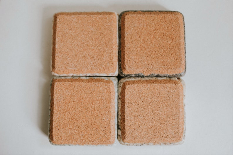 May include: Four square cork coasters with a speckled gray and white pattern. The coasters are made of cork and have a natural, rustic look.