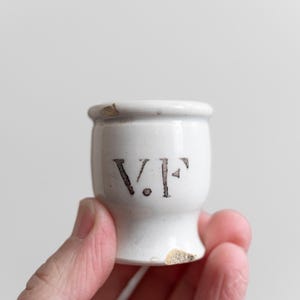 May include: White ceramic jar with a black inscription that reads "V.F."