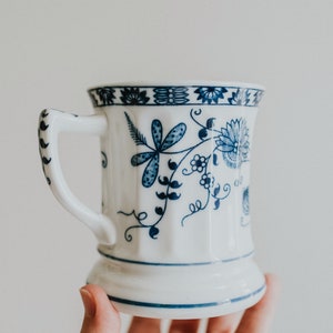 Puede incluir: Una taza de cer&aacute;mica blanca con un dise&ntilde;o floral azul. La taza tiene un asa y una base ancha.