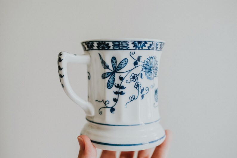 Puede incluir: Una taza de cer&aacute;mica blanca con un dise&ntilde;o floral azul. La taza tiene un asa y una base ancha.