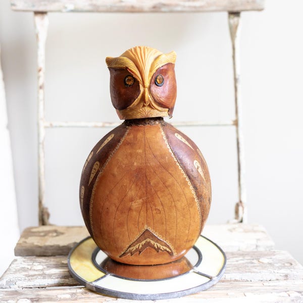 Peut inclure: Sculpture de hibou en bois fait à la main avec un design détaillé. Le hibou a une tête marron clair et un corps marron foncé avec des motifs décoratifs. Il repose sur une base décorative avec une bordure jaune et blanche, créant un objet de décoration unique.