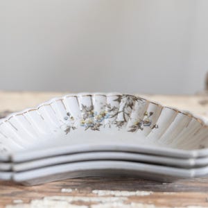May include: A set of three white ceramic crescent-shaped bowls with a floral design and gold trim.