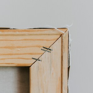 Op de afbeelding: Close-up van een houten frame met nietjes die een canvas aan het frame bevestigen.