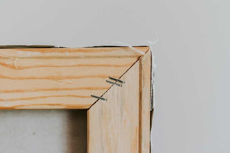 Op de afbeelding: Close-up van een houten frame met nietjes die een canvas aan het frame bevestigen.