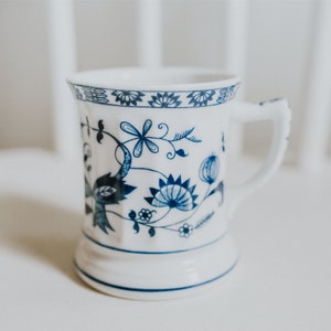 Puede incluir: Una taza de cer&aacute;mica blanca con un dise&ntilde;o floral azul. La taza tiene un asa y una base ancha.
