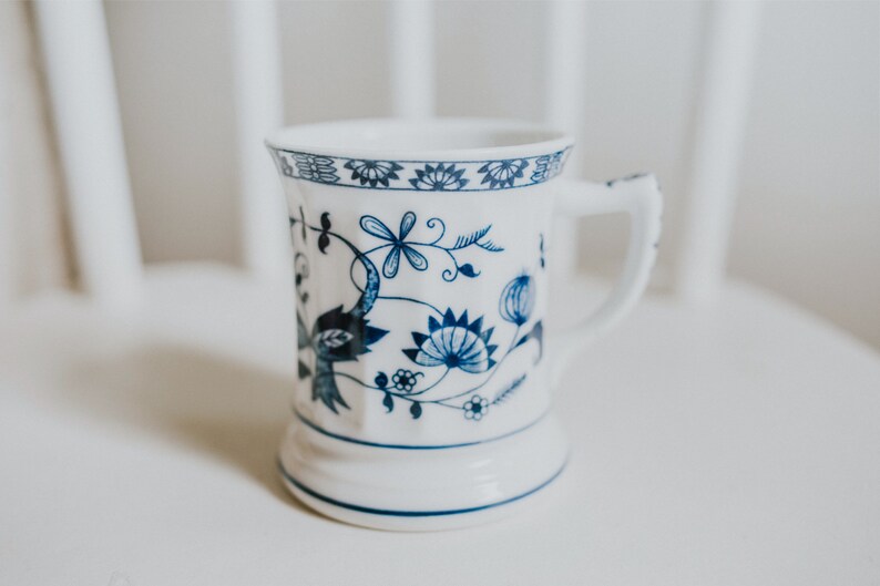 Puede incluir: Una taza de cer&aacute;mica blanca con un dise&ntilde;o floral azul. La taza tiene un asa y una base ancha.