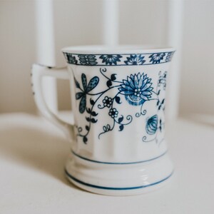 Puede incluir: Una taza de cer&aacute;mica blanca con un patr&oacute;n floral azul. La taza tiene un asa y una base ancha.