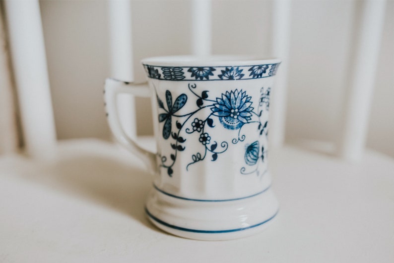 Puede incluir: Una taza de cer&aacute;mica blanca con un patr&oacute;n floral azul. La taza tiene un asa y una base ancha.