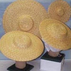 Puede incluir: Se muestran cuatro sombreros de paja de diferentes tamaños. Los sombreros tienen alas anchas y un color marrón claro natural. Los sombreros están sobre expositores, destacando su forma y diseño.