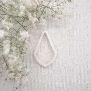 May include: White plastic cookie cutter shaped like a teardrop with a pointed tip.