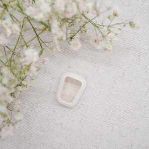 May include: White ceramic ring with a rectangular shape and a smooth, matte finish.