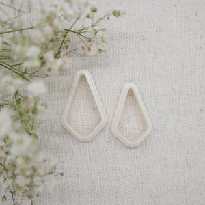May include: Two white geometric shaped earrings with a diamond-like design.