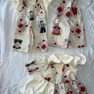 May include: Three sets of doll clothes featuring a white background with red hearts and a pattern of people in red and green clothing. The clothes are made of a soft, white fabric and have a vintage look.