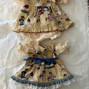 Puede incluir: Dos conjuntos de ropa para muñecas, ambos en tela amarilla con patrón de rombos y estampado de niños jugando. El conjunto superior tiene botones rojos y dobladillo con volantes, el inferior incluye una cinta azul y encaje blanco.