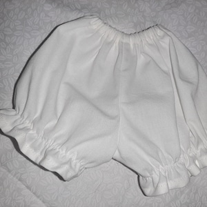 May include: White cotton baby bloomers with a ruffled edge.