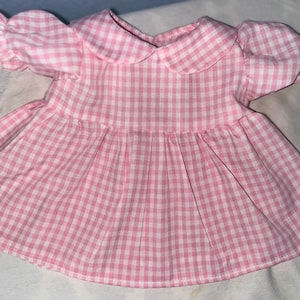 Puede incluir: Un vestido de cuadros vichy rosa y blanco con cuello de Peter Pan y mangas abullonadas.