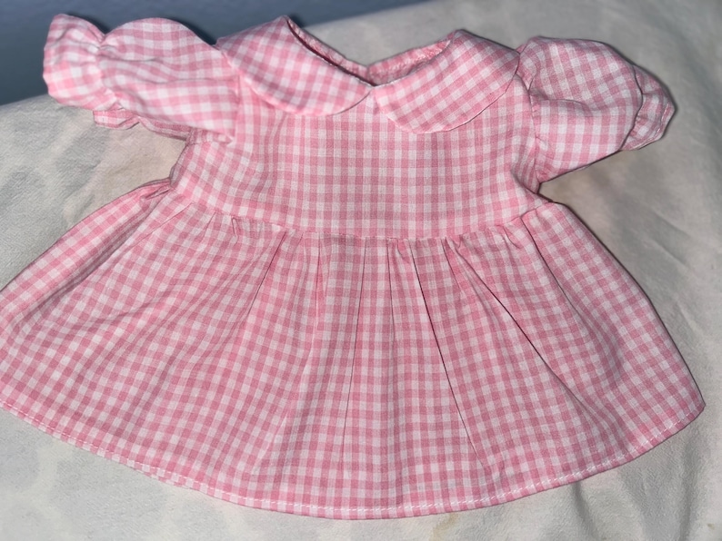 Puede incluir: Un vestido de cuadros vichy rosa y blanco con cuello de Peter Pan y mangas abullonadas.