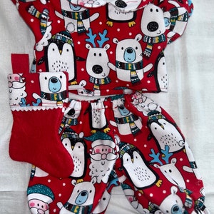 Pode incluir: Pijama vermelho e branco com tema natalino com pinguins, ursos polares, renas e Papai Noel. O pijama tem uma parte superior de manga comprida e calças com uma borda branca.