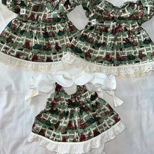 May include: Two green and white dresses with a bear and fence print, and a white dress with a matching print. The dresses have white lace trim and are labeled #1 and #2.