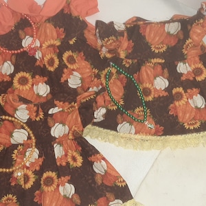 May include: Two brown and orange dresses with a pumpkin and sunflower print. One dress has a lace trim and the other has a solid orange top.