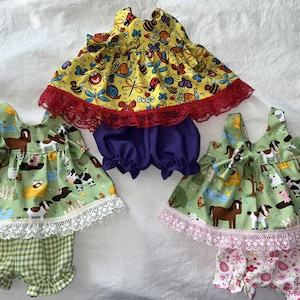 May include: Three sets of baby clothing. One set features a yellow top with a red lace trim and purple shorts. The other two sets have green tops with farm animal prints and white lace trim, paired with checkered and floral shorts.