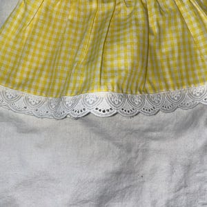 Peut inclure: Un tissu vichy jaune et blanc avec une bordure en dentelle blanche. Le tissu est froncé, créant un effet volanté. La bordure en dentelle présente un bord festonné.