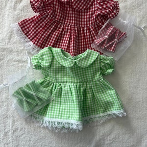 以下が含まれることがあります： 白いレースのトリムと合わせたボウが付いた、ギンガムチェックのドレス2着。上のドレスは赤と白、下のドレスは緑と白です。