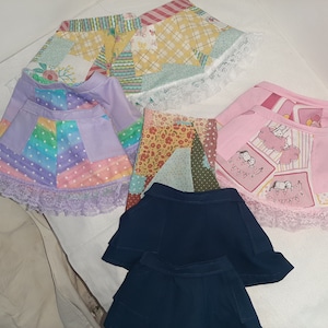May include: Five different skirts with lace trim. The skirts are made of patchwork fabric with various patterns and colors, including pink, blue, green, yellow, and white.