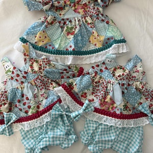 May include: Three doll outfits featuring a patchwork pattern of strawberries, light blue gingham, and floral prints. The top garment is a dress with a teal button and trim. The two bottom garments are sets consisting of a top and matching bloomers.