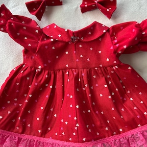 May include: Red dress with white and pink hearts, a pink lace trim, and two red bows.