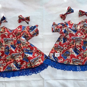 Pode incluir: Dois vestidos de Natal vermelhos e azuis com uma borda de renda branca e azul. Cada vestido tem um laço e o número #1 e #2 na frente.