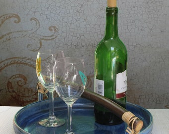 May include: A blue ceramic serving tray with a wooden handle and two wine glasses and a bottle of wine on top.