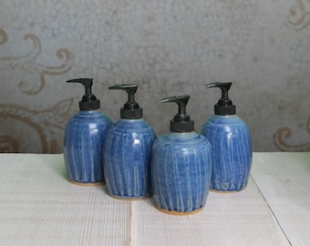 May include: Four blue ceramic soap dispensers with black pump tops. The dispensers have a light blue glaze with a darker blue stripe pattern.