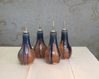 May include: Four ceramic oil and vinegar bottles with silver tops. The bottles are brown with blue glaze and have a teardrop shape.