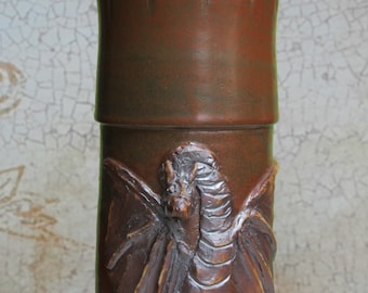 May include: A brown ceramic jar with a dragon design. The jar has a lid with a wooden handle and a brown and tan rope wrapped around it.