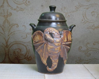 May include: A black ceramic jar with a lid, featuring a detailed brown and tan dragon design.