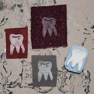 May include: An artistic arrangement featuring four fabric squares and a blue block, each displaying a white tooth design. The squares vary in color, including red, burgundy, and gray, with the tooth design printed on each.