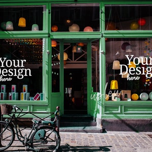 May include: A green storefront with two large windows displaying colorful decorations and the text "Your Design here". A bicycle is parked in front of the store.