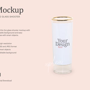 May include: A mockup of a 2 ounce glass shooter with a gold rim. The glass is clear and has a white background with the text "Your Design here" in black. The background is a light pink color.