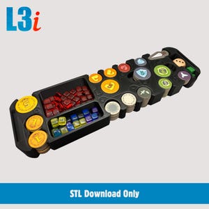 Op de afbeelding: Een zwarte plastic bordspel-organizer met meerdere vakken gevuld met diverse spelonderdelen, waaronder rode, blauwe en gele doorschijnende blokjes, gestapelde ronde fiches met iconen, en de tekst L3i en STL Download Only.