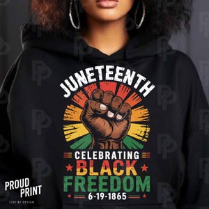 May include: Black hoodie with a graphic celebrating Juneteenth. The design features the word "Juneteenth" above a clenched fist within a colorful sunburst. Below, it reads "Celebrating Black Freedom" and "6-19-1865".