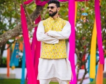 Könnte beinhalten: Ein Mann trägt eine weiße Kurta und eine gelbe Weste mit Blumenmuster. Er trägt eine Sonnenbrille und hat einen Bart. Er steht vor einem bunten Hintergrund aus Stoff.